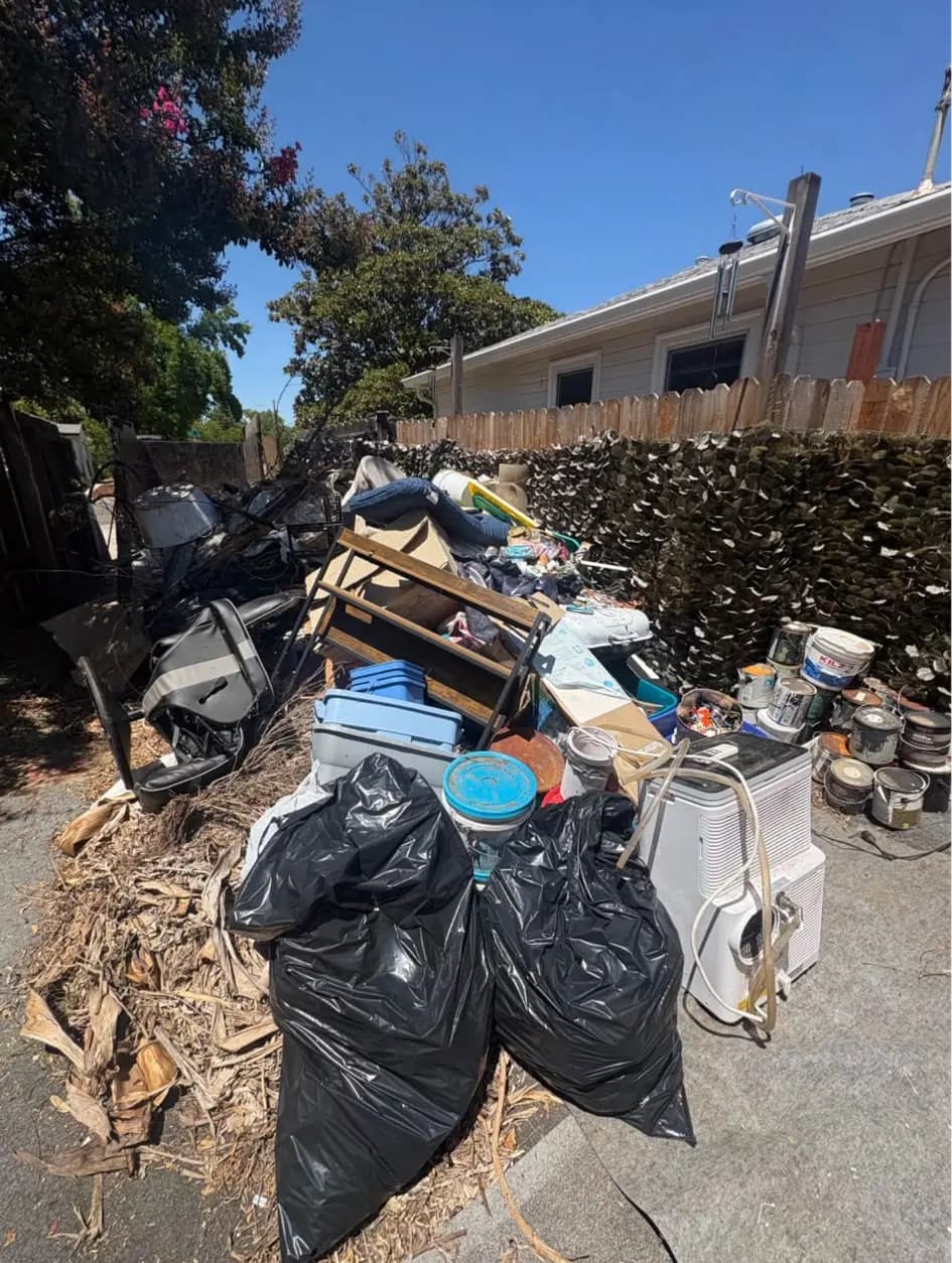 Driveway pile of trash bags, palm fronds, a shelf, plastic bins and a portable air conditioner