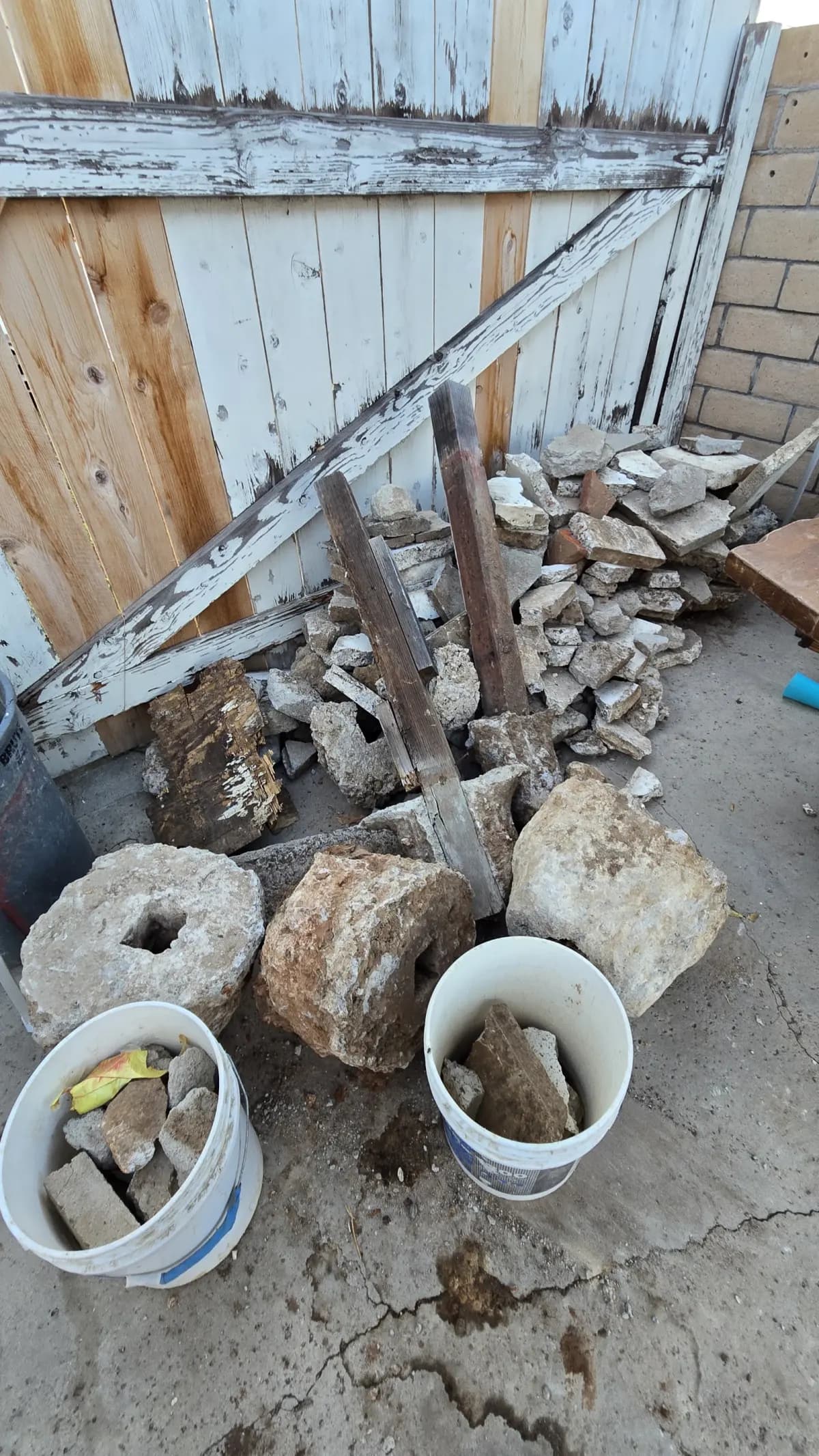 Broken concrete chunks, rocks in buckets and old fence boards stacked for removal